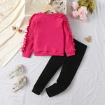 Bright pink ruffle-sleeve sweatshirt with black heart graphic paired with black leggings — cute, cozy outfit for girls.