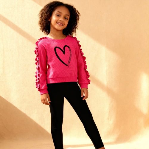 Bright pink ruffle-sleeve sweatshirt with black heart graphic paired with black leggings — cute, cozy outfit for girls.