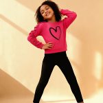 Bright pink ruffle-sleeve sweatshirt with black heart graphic paired with black leggings — cute, cozy outfit for girls.