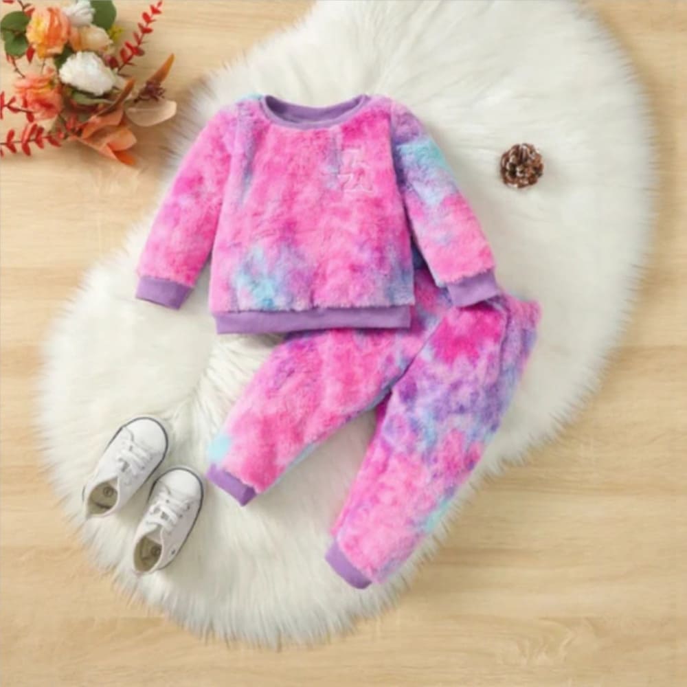 A vibrantly colored toddler girls' fuzzy loungewear set in tie-dye shades of pink, purple, and blue. The set includes a long-sleeve crewneck pullover top and matching jogger pants with elastic cuffs, laid flat on a white fluffy rug.