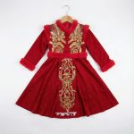Girl wearing red velvet dress with gold embroidery and faux fur trim
